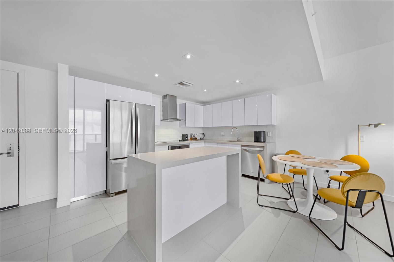 A modern kitchen features white cabinetry, stainless steel appliances, a central island, and yellow chairs — 1600 NE 1st Ave # 2318, Miami FL 33132, MIAMI, FL