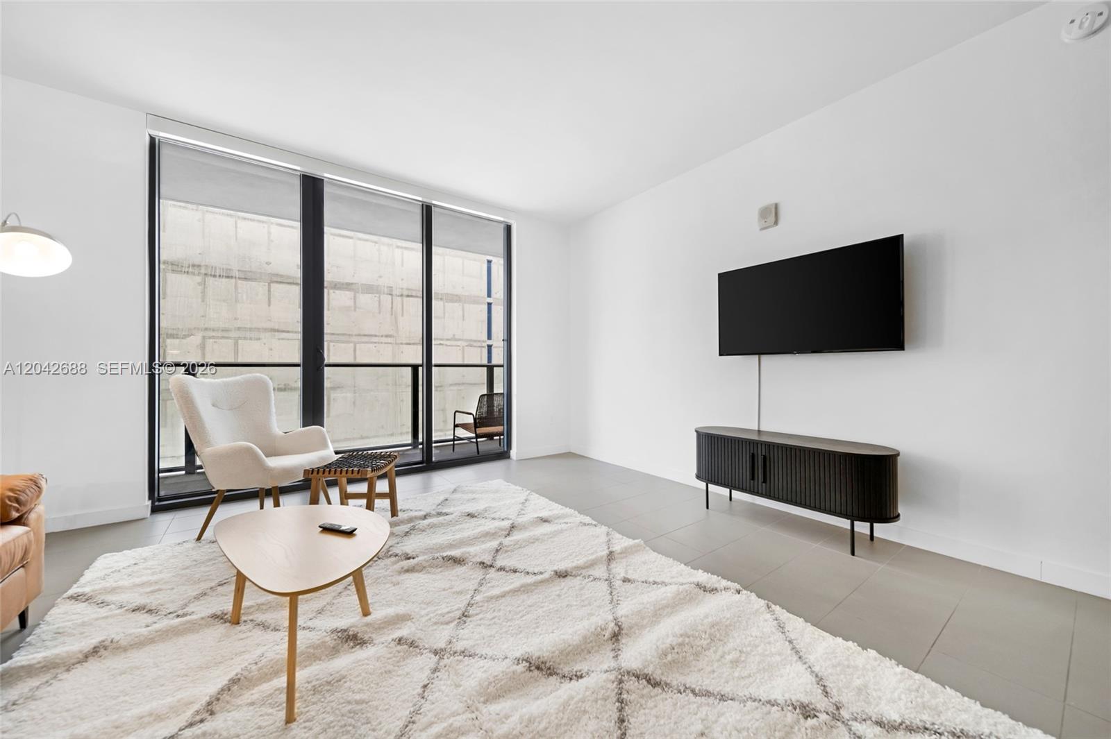 A modern living room features a white rug, a wall-mounted television, and floor-to-ceiling windows — 1600 NE 1st Ave # 2318, Miami FL 33132, MIAMI, FL