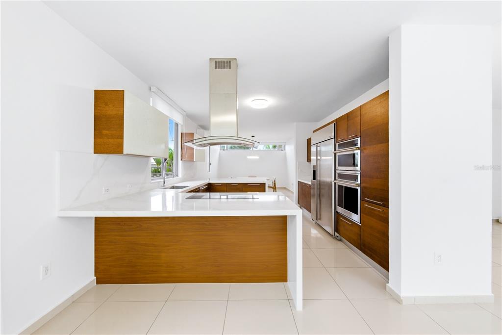 A modern kitchen features wood cabinetry, white countertops, a central island, and stainless steel appliances — 70 CALLE AQUAMARINA, SAN JUAN, PR