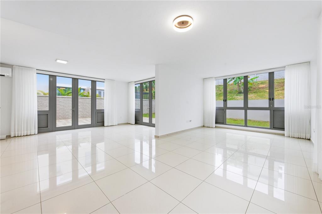 A bright, empty room with white tile floors, large windows, and glass doors leading outside — 70 CALLE AQUAMARINA, SAN JUAN, PR