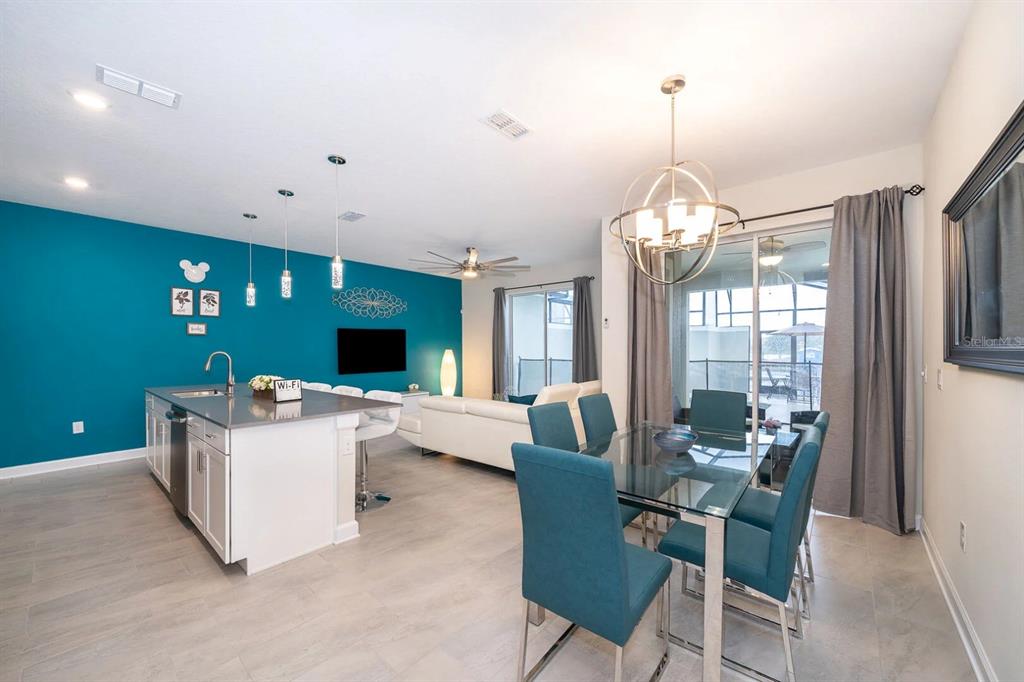 An open-concept kitchen and dining area featuring teal accent walls and modern light fixtures — 4830 DEDICATION STREET, KISSIMMEE, FL