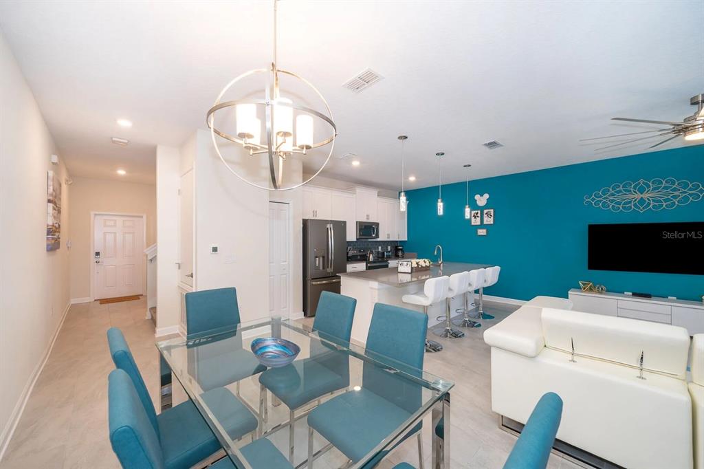 An open-concept dining and living area features a glass table, kitchen island, and teal wall — 4830 DEDICATION STREET, KISSIMMEE, FL
