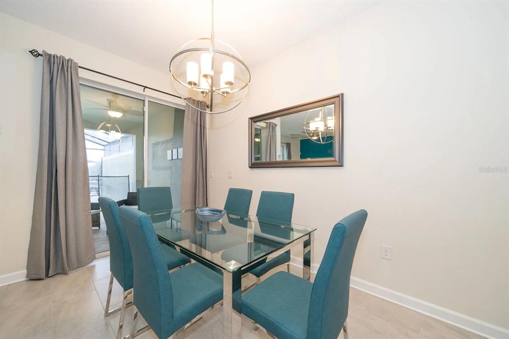 A dining room features a glass table, six teal chairs, a chandelier, and sliding glass doors — 4830 DEDICATION STREET, KISSIMMEE, FL