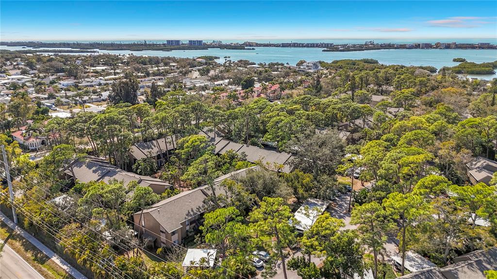 An aerial view shows multi-story residential buildings nestled among dense trees near a large bay — 1717 PELICAN COVE ROAD UNIT GL434, SARASOTA, FL