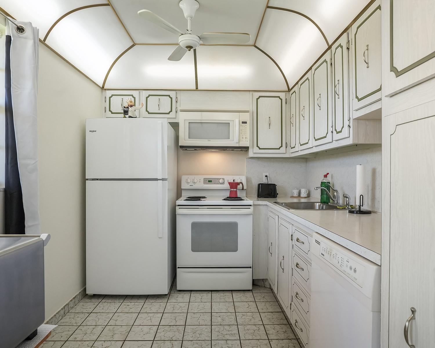 A galley kitchen features white appliances, light-colored cabinets with green trim, and a vaulted ceiling — 2615 NE 3rd Court # 314, Boynton Beach FL 33435, BOYNTON BEACH, FL