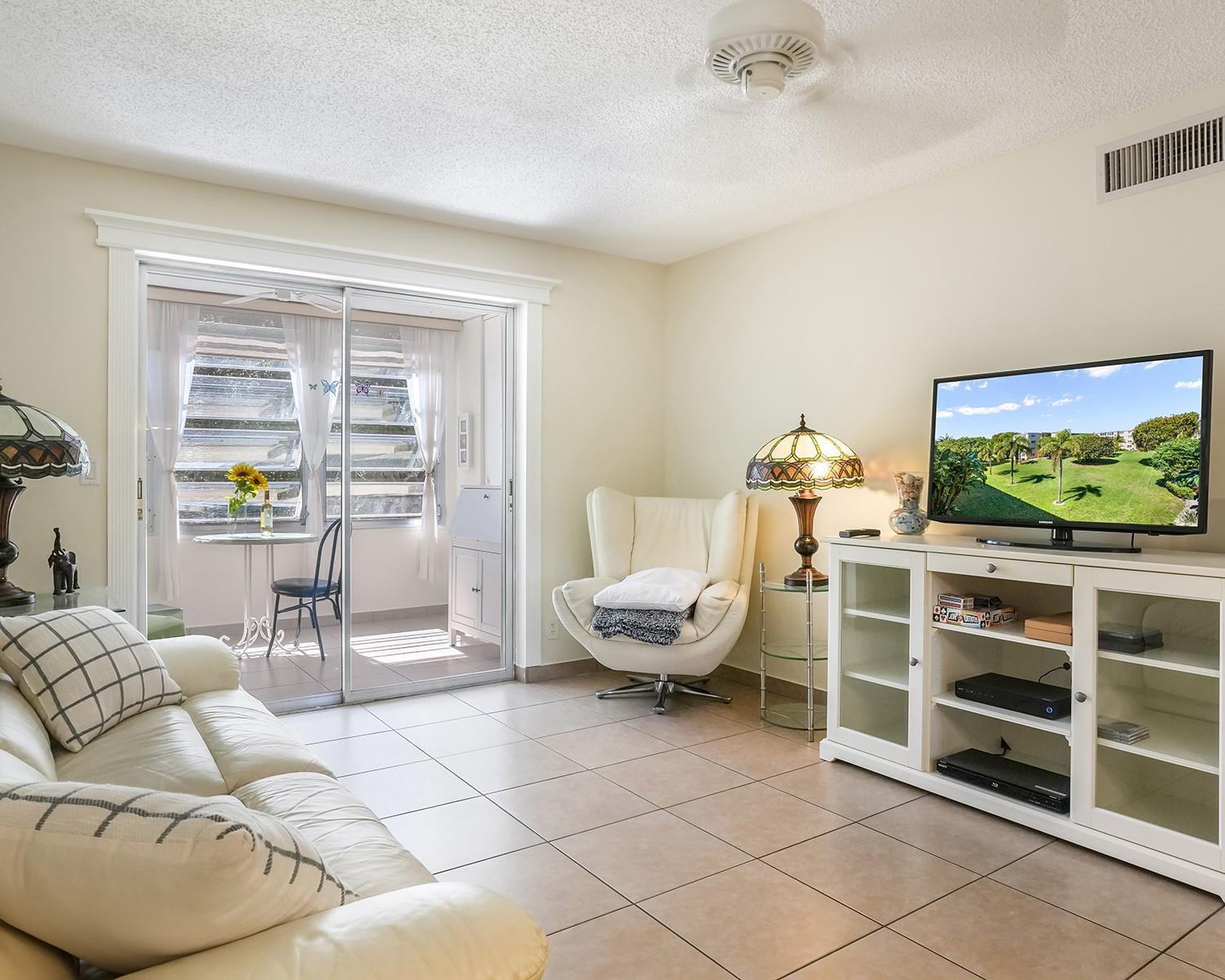 A living room with tile floors, a white sofa, a swivel chair, and a sliding door — 2615 NE 3rd Court # 314, Boynton Beach FL 33435, BOYNTON BEACH, FL