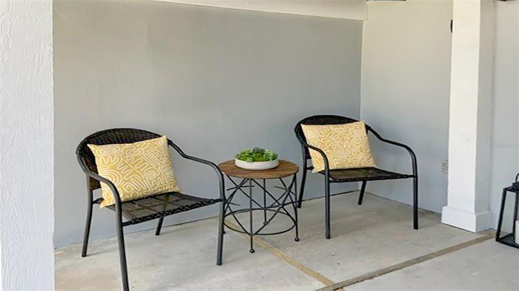 Two black chairs with yellow patterned pillows flank a small round table on a patio — 1230 SIESTA BAYSIDE DRIVE UNIT 1230-D, SARASOTA, FL