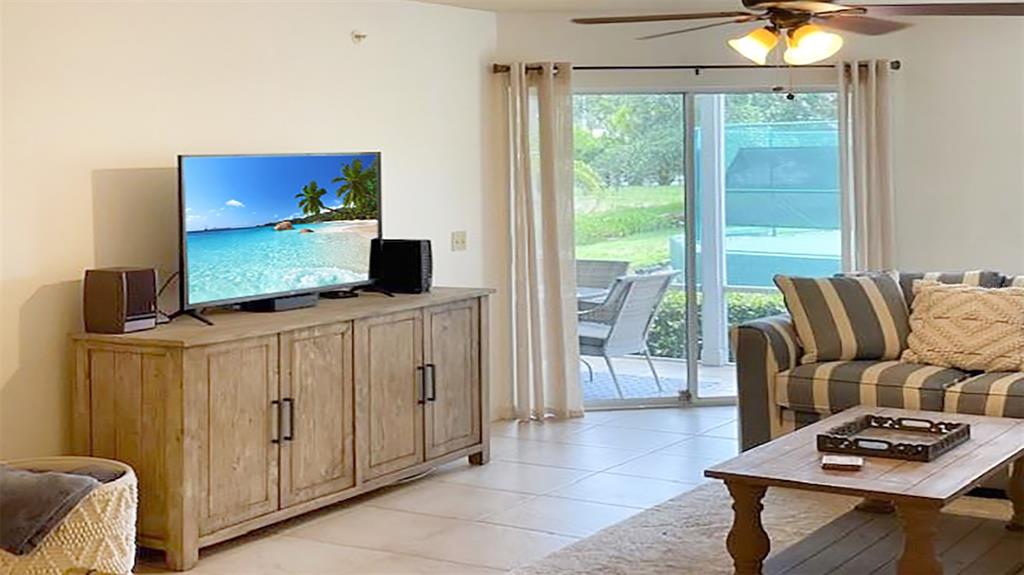 A living room features a wooden media console, a striped sofa, and a sliding glass door — 1230 SIESTA BAYSIDE DRIVE UNIT 1230-D, SARASOTA, FL