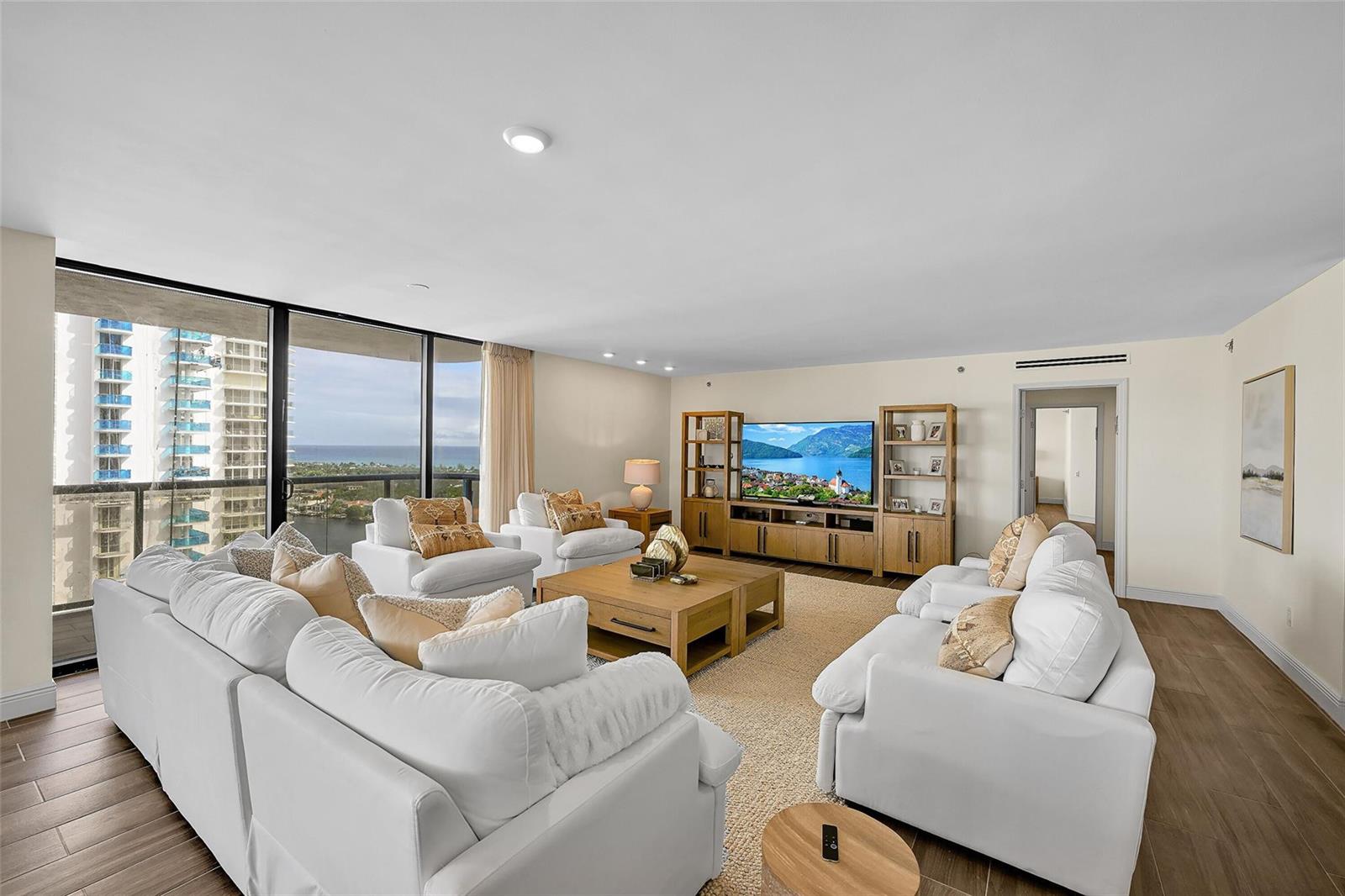 A living room features white sofas, a wooden coffee table, and floor-to-ceiling windows with ocean views — 19667 Turnberry Way, Miami FL 33180, MIAMI, FL