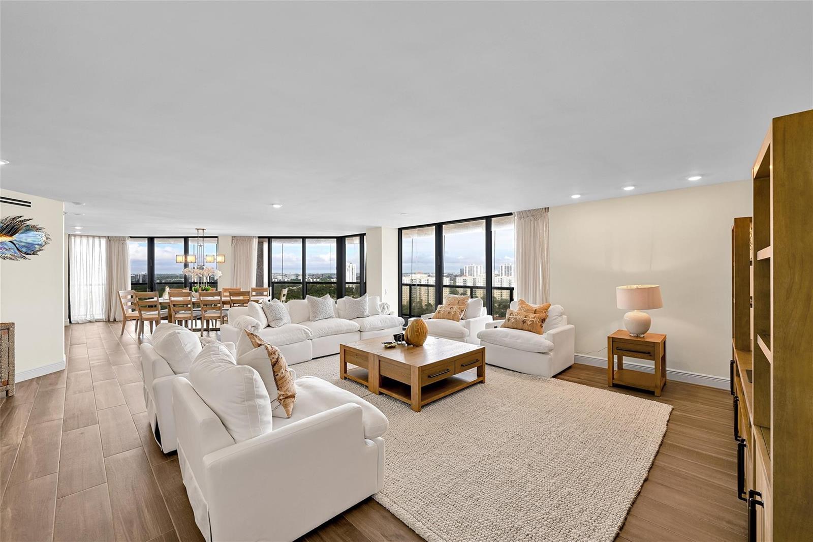 A bright, open-concept living and dining area features white furniture, wood flooring, and floor-to-ceiling windows — 19667 Turnberry Way, Miami FL 33180, MIAMI, FL