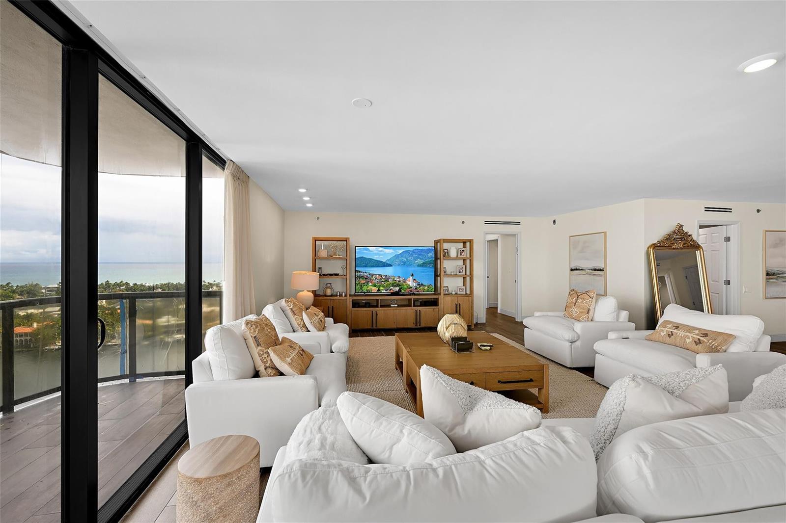 A bright living room features white sofas, a wooden coffee table, and a balcony view — 19667 Turnberry Way, Miami FL 33180, MIAMI, FL