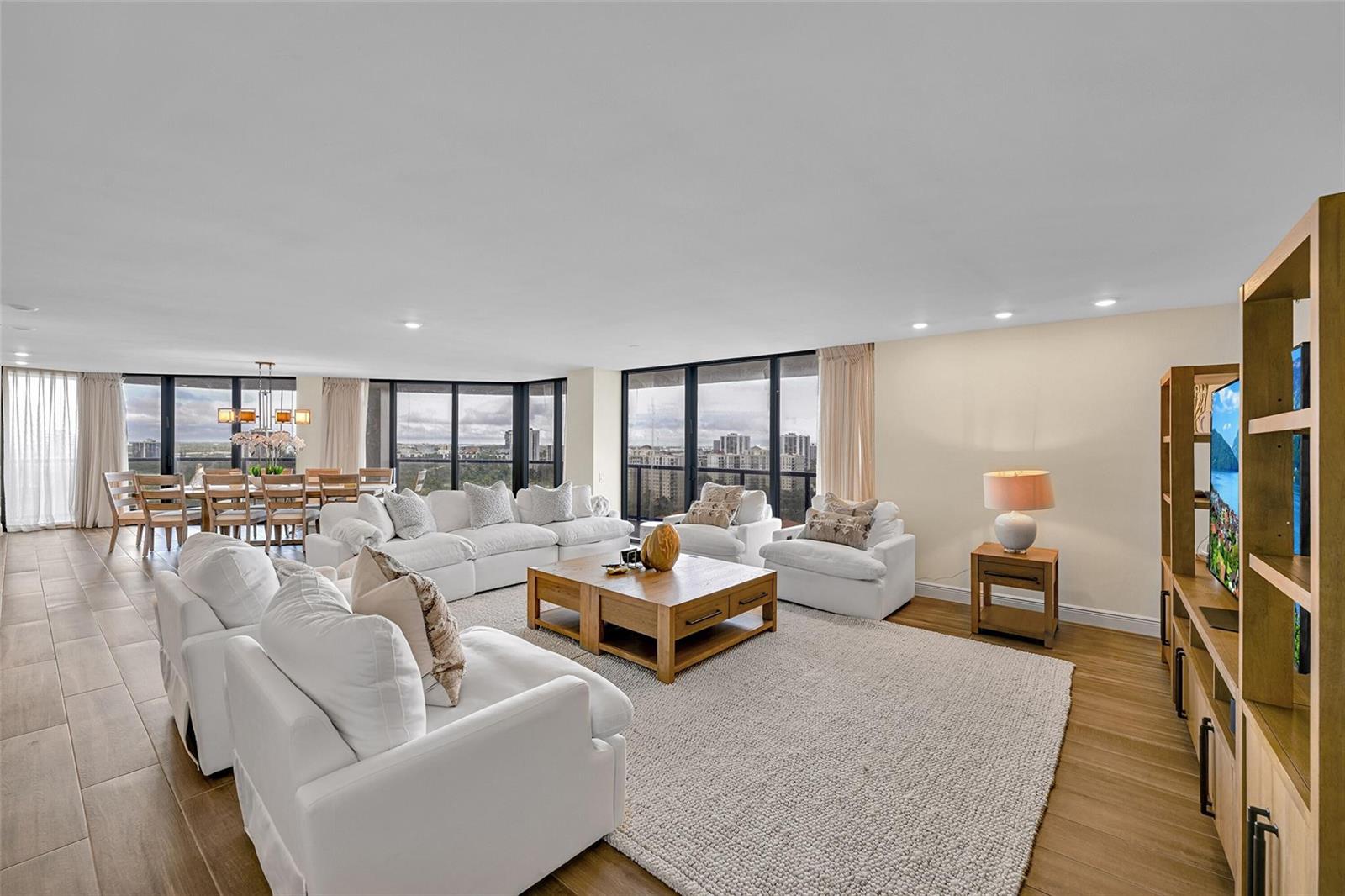 A bright living and dining area features white furniture, wood flooring, and floor-to-ceiling windows — 19667 Turnberry Way, Miami FL 33180, MIAMI, FL