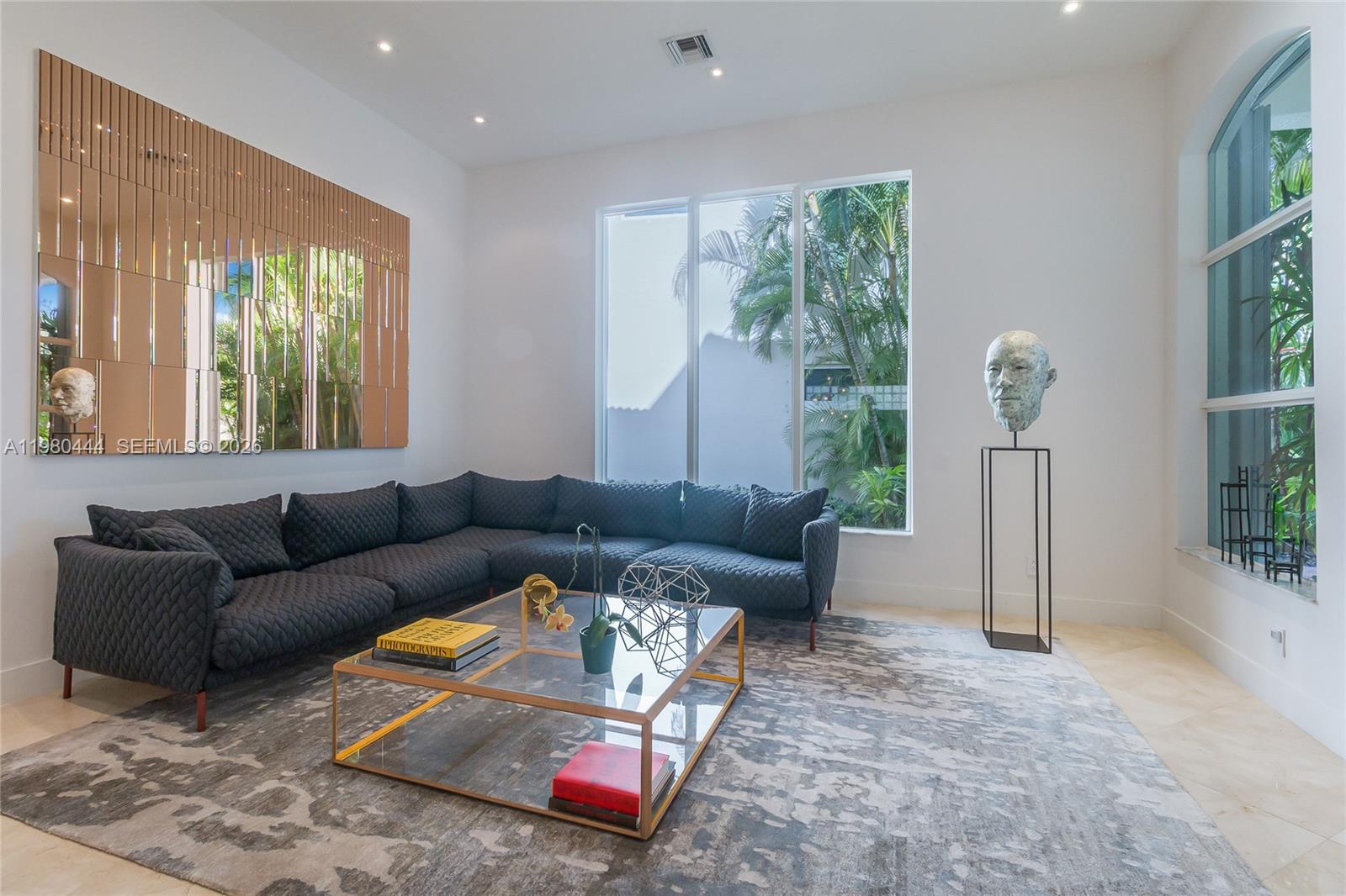 A modern living room features a dark quilted sectional, glass coffee table, and large windows — 1651 NE 196th St, Miami FL 33179, MIAMI, FL