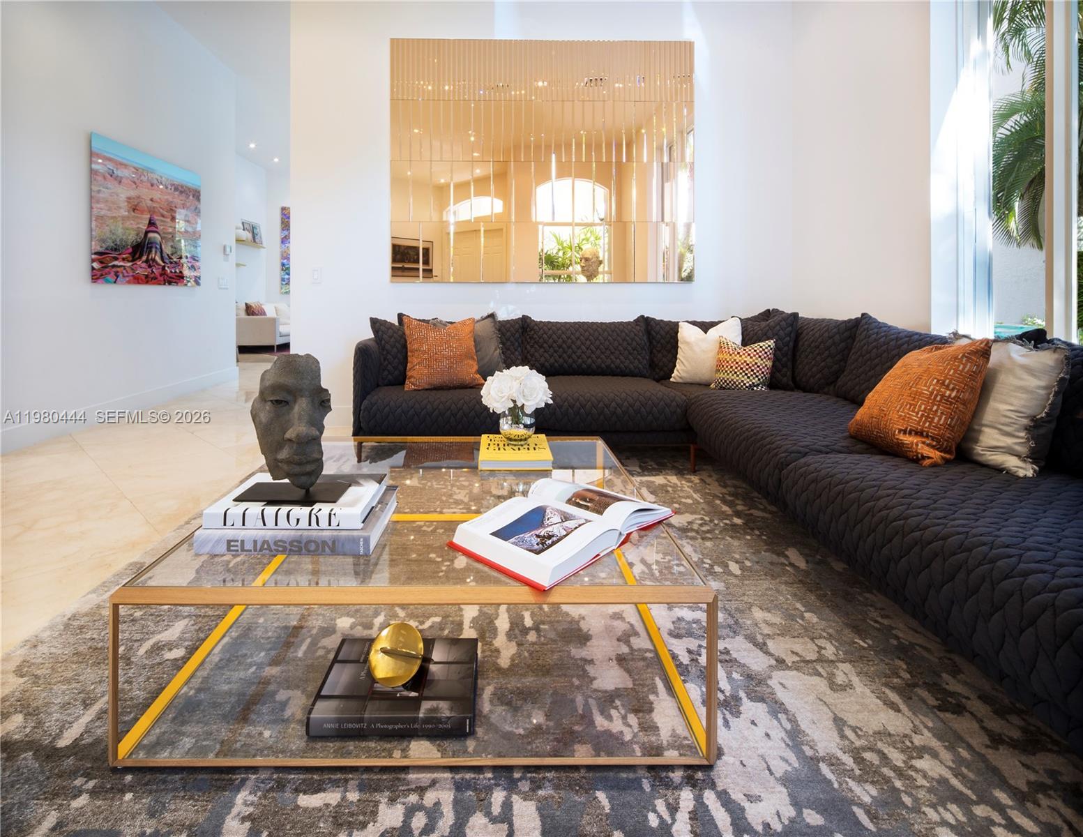 A modern living room features a quilted dark sectional sofa, glass coffee table, and mirror — 1651 NE 196th St, Miami FL 33179, MIAMI, FL