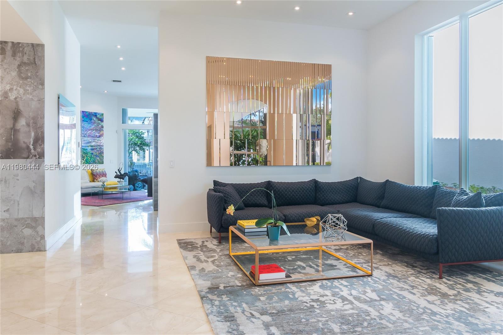 A modern living room features a dark quilted sectional sofa, a glass coffee table, and a mirror — 1651 NE 196th St, Miami FL 33179, MIAMI, FL