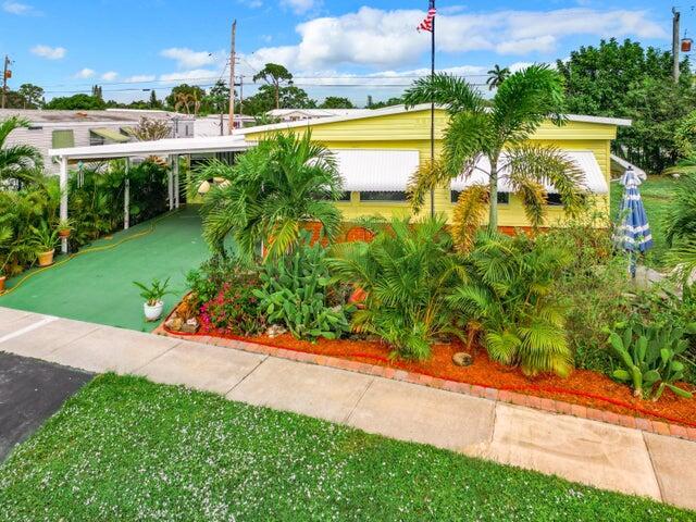 A yellow mobile home with a green carport and lush landscaping sits behind a sidewalk — 4215 Meadow View Drive, Boynton Beach FL 33436, BOYNTON BEACH, FL