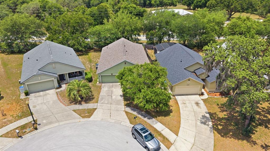 An aerial view shows three suburban houses with driveways situated along a curved street — 3002 LORIMER CT, GROVELAND, FL