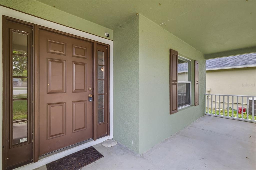 A covered front porch features a brown door with sidelights and a window with shutters — 3002 LORIMER CT, GROVELAND, FL