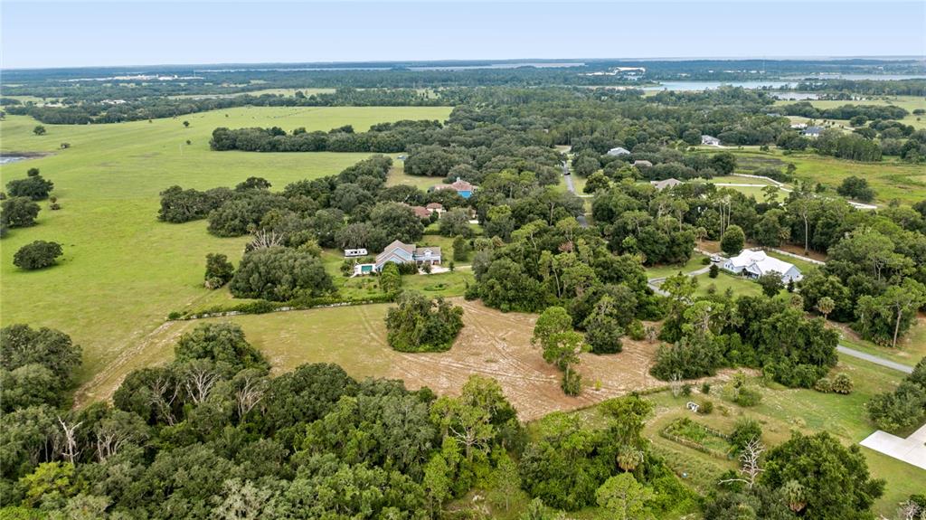 An aerial view shows a rural landscape with scattered houses, dense trees, and open fields — TROTTING HORSE LANE, TAVARES, FL