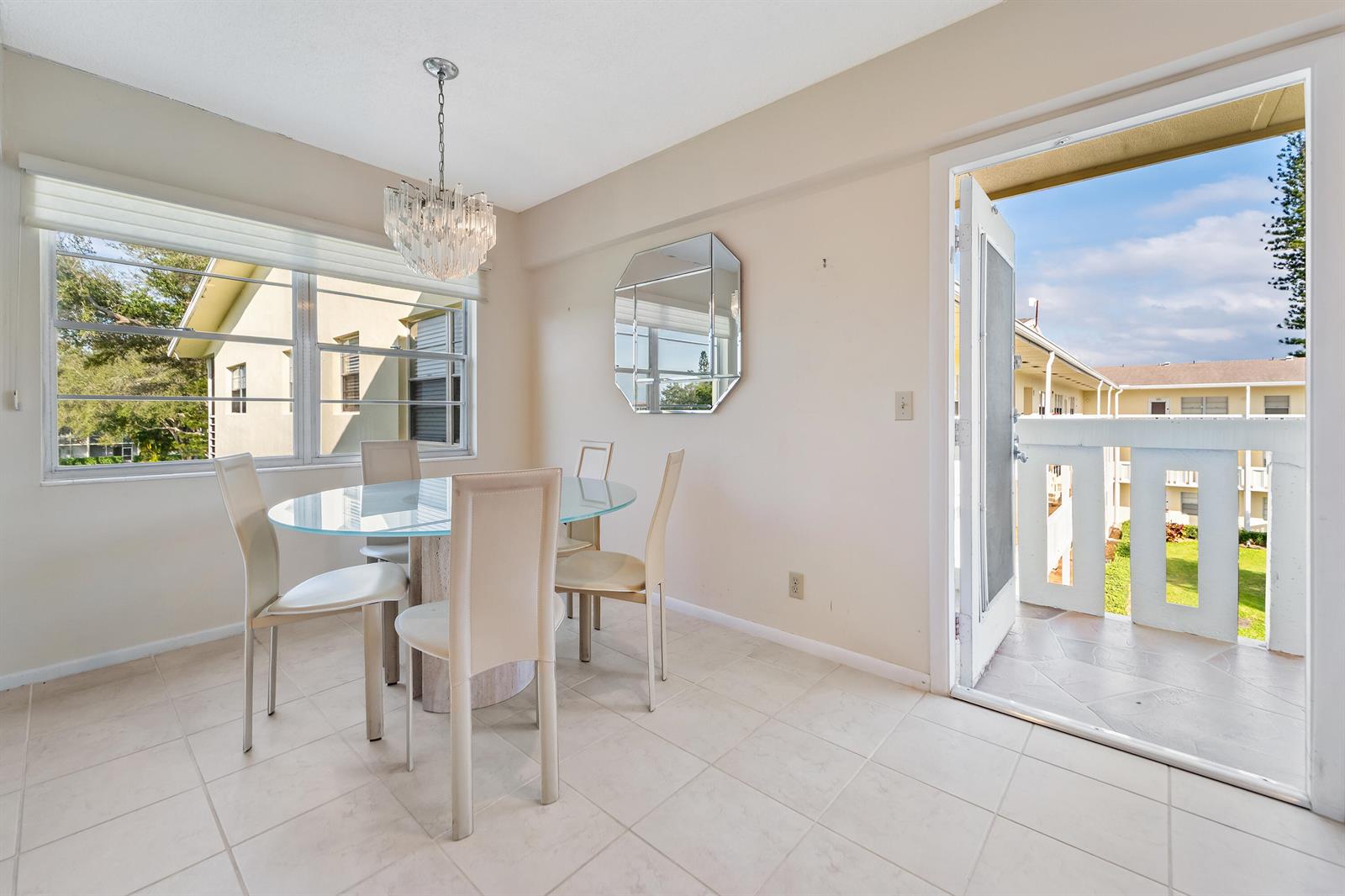 A dining area features a glass table, four chairs, a chandelier, and a balcony door — 200 Dorset E, Boca Raton FL 33434, BOCA RATON, FL
