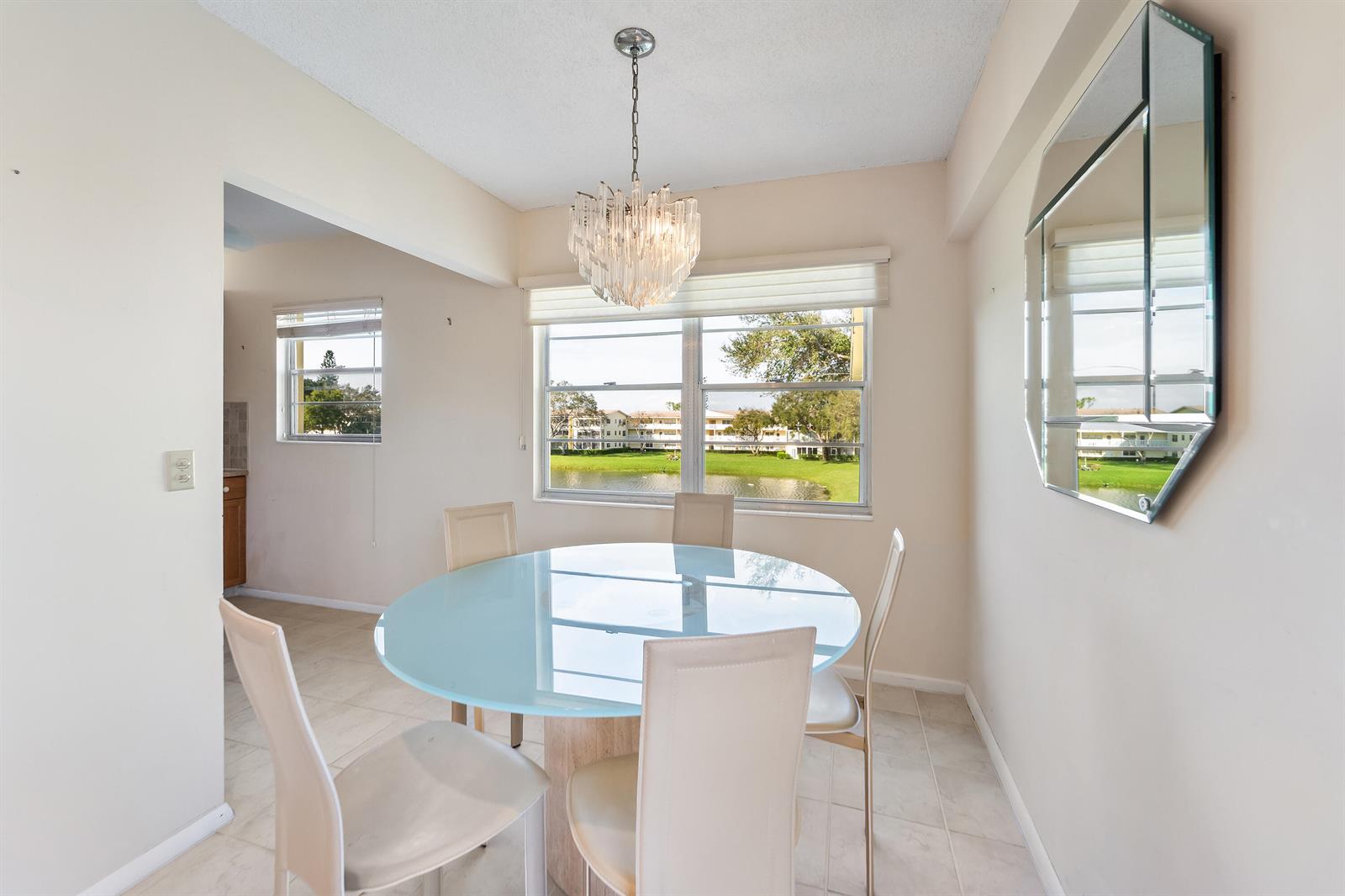 A dining area features a round glass table, four chairs, a chandelier, and a mirror — 200 Dorset E, Boca Raton FL 33434, BOCA RATON, FL