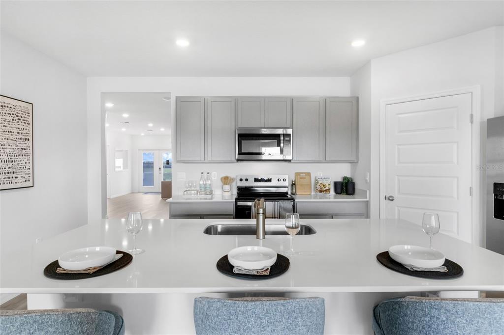 A kitchen island with white countertops sits in front of gray cabinets and stainless appliances — 7864 FORREST FOX WAY, LAKELAND, FL