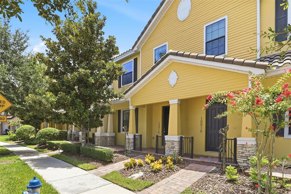 A yellow two-story townhouse with stone accents, a covered porch, and a brick walkway — 10016 EAGLE CREEK CENTER BOULEVARD, ORLANDO, FL