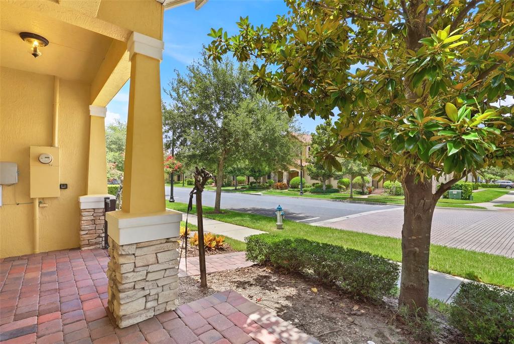 A paved front porch with a stone-based pillar overlooks a suburban street and green space — 10016 EAGLE CREEK CENTER BOULEVARD, ORLANDO, FL