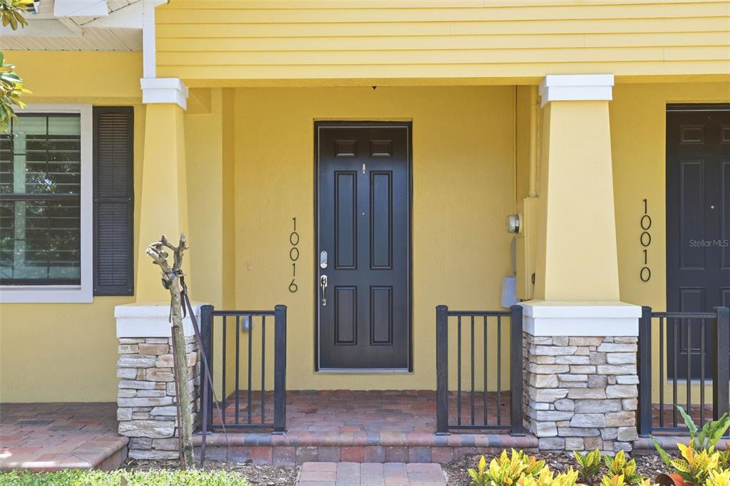 A yellow house exterior features a dark front door, stone-based columns, and a brick porch — 10016 EAGLE CREEK CENTER BOULEVARD, ORLANDO, FL