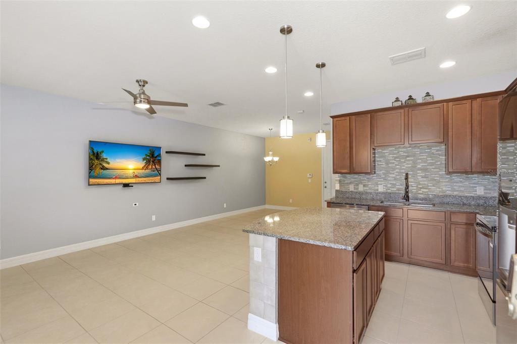 A kitchen with granite countertops and brown cabinets opens to a living area with tile — 10016 EAGLE CREEK CENTER BOULEVARD, ORLANDO, FL