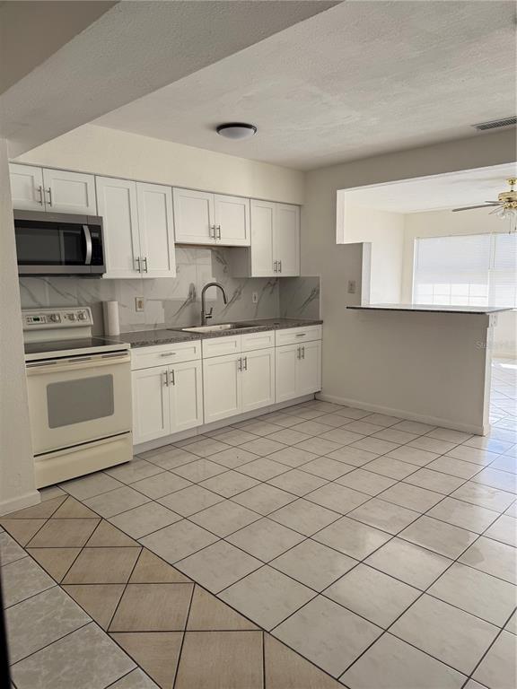 A kitchen features white cabinets, stainless steel appliances, granite countertops, and light-colored tile flooring — 4737 56TH AVENUE N, ST PETERSBURG, FL