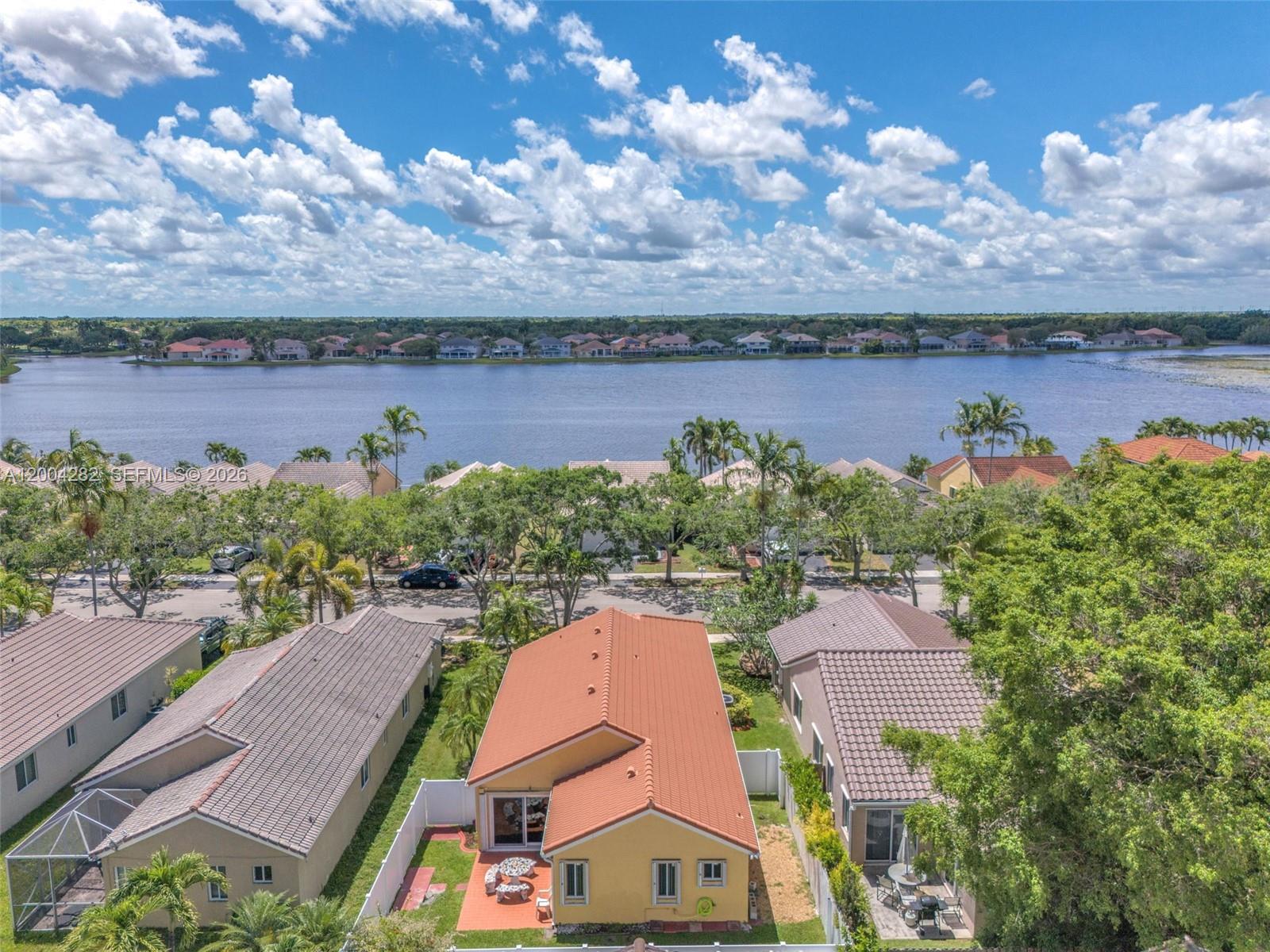 An aerial view shows a yellow house with a red roof overlooking a large lake — 1600 Salerno Cir, Weston FL 33327, WESTON, FL