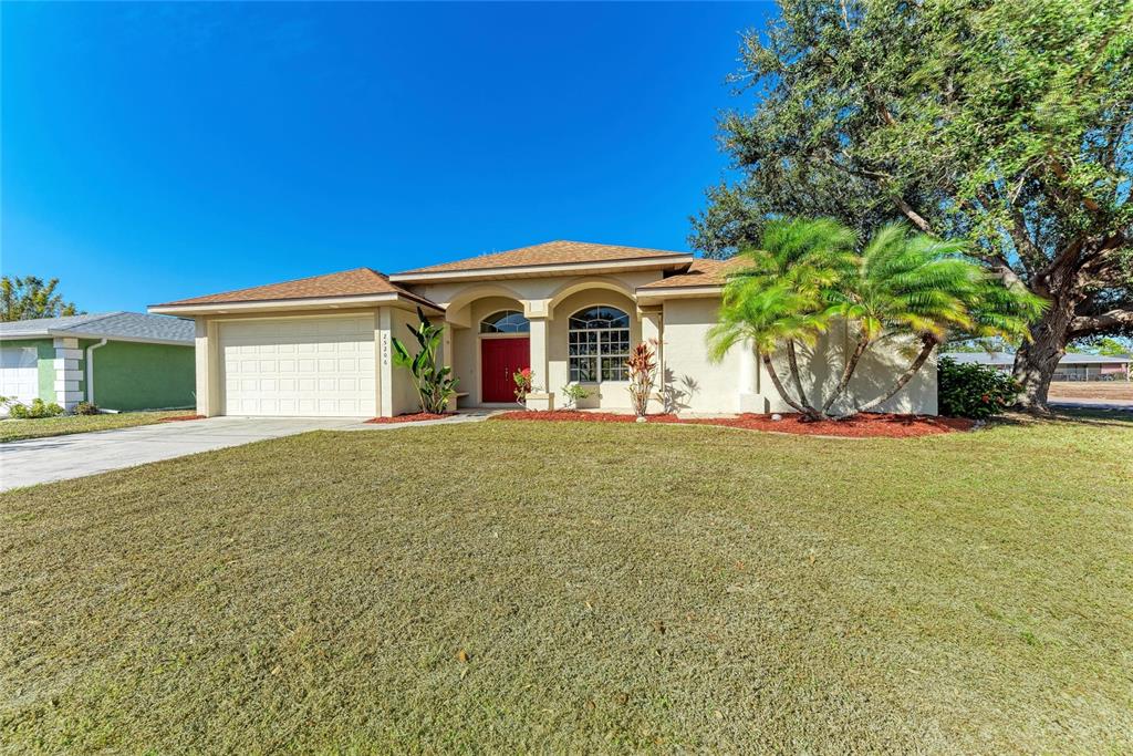 A single-story house with a tan stucco exterior, a two-car garage, and palm trees — 25206 NOCTURNE LANE, PUNTA GORDA, FL