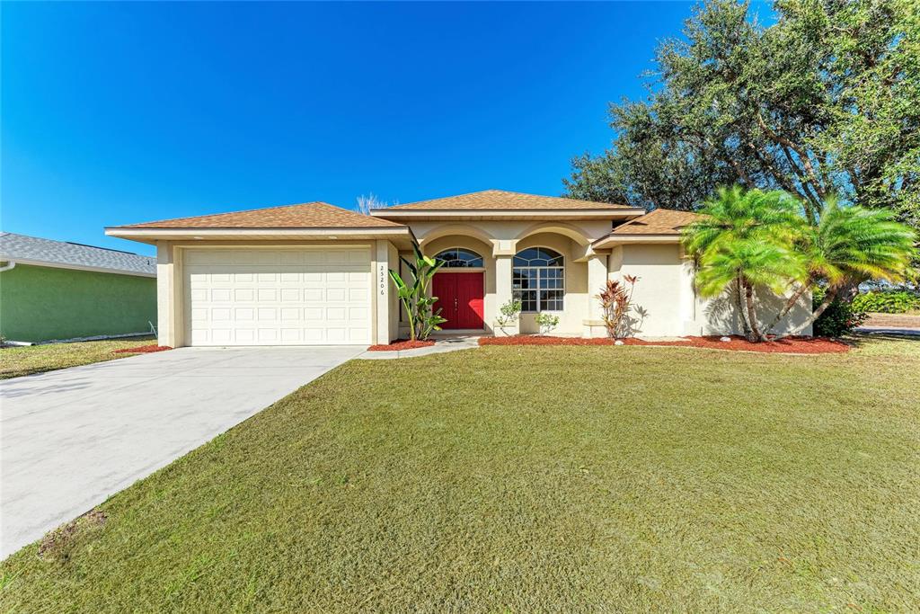 A single-story house with a beige exterior, red front door, and a two-car garage — 25206 NOCTURNE LANE, PUNTA GORDA, FL