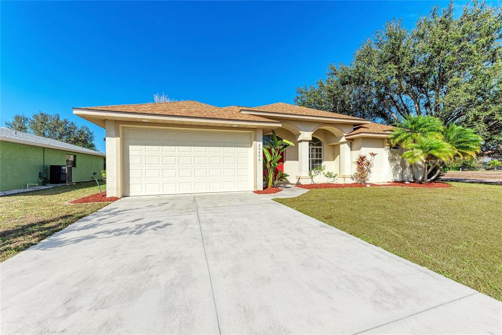 A single-story house with a beige stucco exterior, a two-car garage, and a red door — 25206 NOCTURNE LANE, PUNTA GORDA, FL