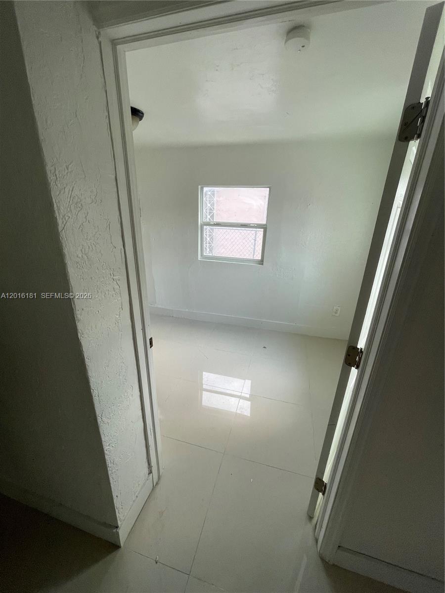 A small, empty room with white walls and light-colored tile flooring viewed through a doorway — MIAMI, FL