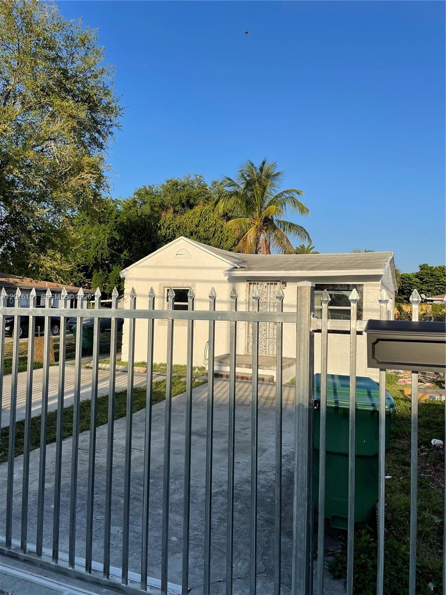 A white, single-story house is viewed from behind a metal security fence — MIAMI, FL