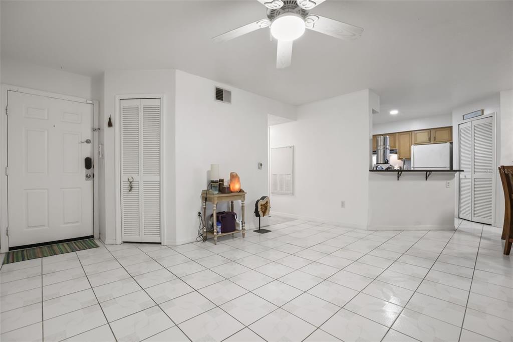 A bright, open-concept living area features white tile flooring, a ceiling fan, and a kitchen — 4690 SUSSEX TERRACE UNIT 103, ORLANDO, FL