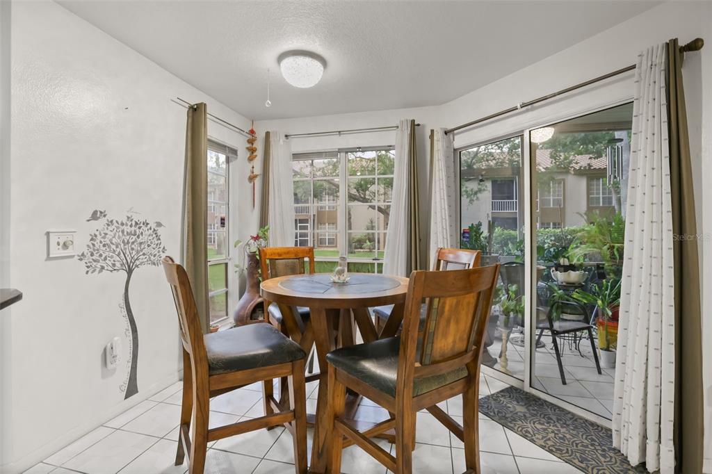 A dining area with a round wooden table, four chairs, tile flooring, and sliding glass doors — 4690 SUSSEX TERRACE UNIT 103, ORLANDO, FL