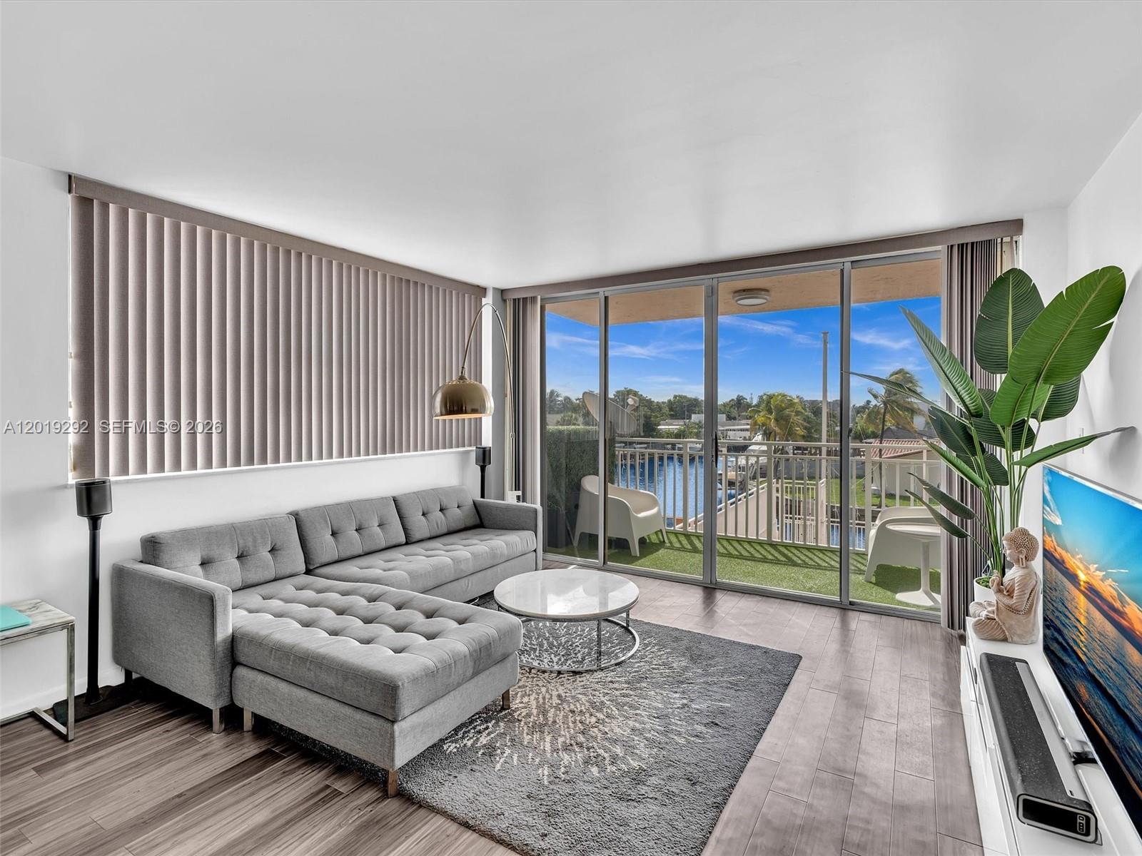 A living room features a grey sectional sofa, a round coffee table, and a balcony view — 2450 NE 135th St # 201, North Miami FL 33181, NORTH MIAMI, FL
