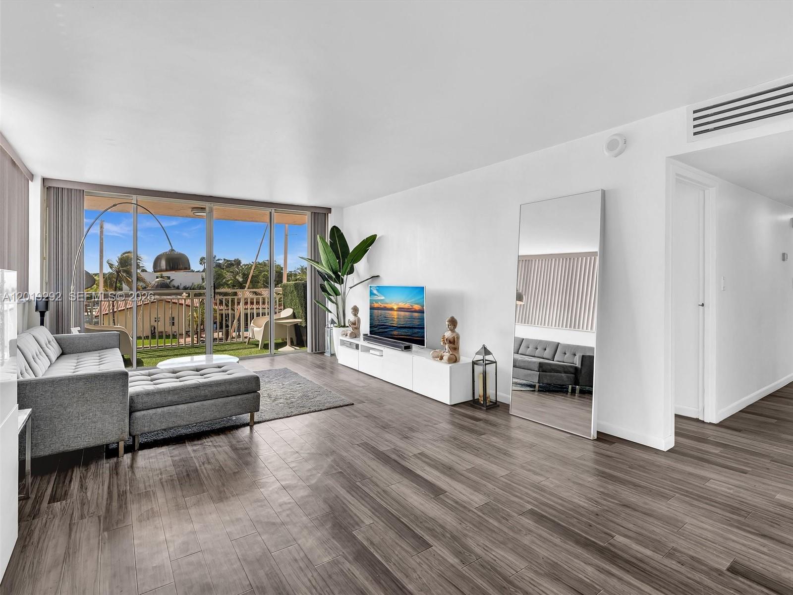 A living room features gray wood-look flooring, a sectional sofa, and a balcony with outdoor seating — 2450 NE 135th St # 201, North Miami FL 33181, NORTH MIAMI, FL