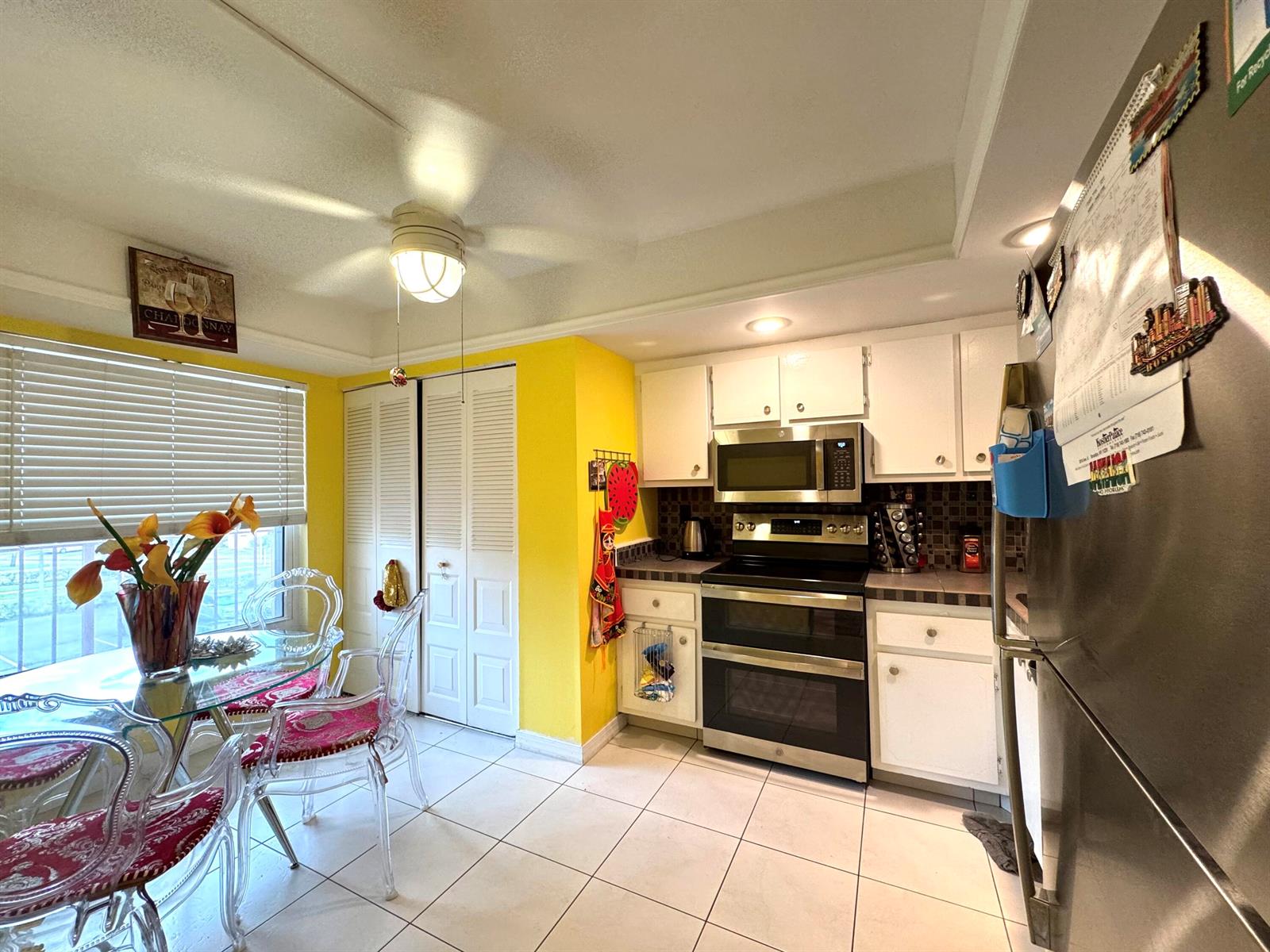 A kitchen with white cabinets, stainless steel appliances, yellow walls, and a glass dining table — 14671 Bonaire Boulevard # 304, Delray Beach FL 33446, DELRAY BEACH, FL