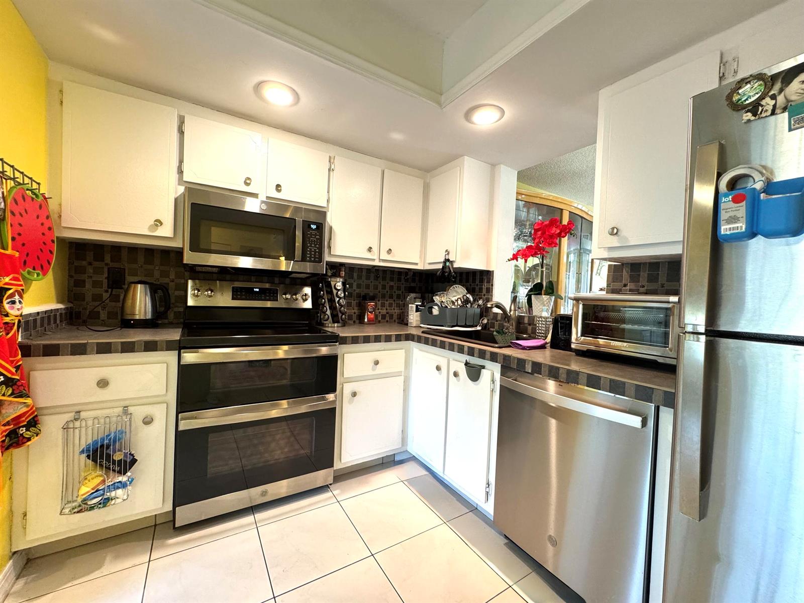 A kitchen features white cabinets, stainless steel appliances, dark tile backsplashes, and light floor tiles — 14671 Bonaire Boulevard # 304, Delray Beach FL 33446, DELRAY BEACH, FL