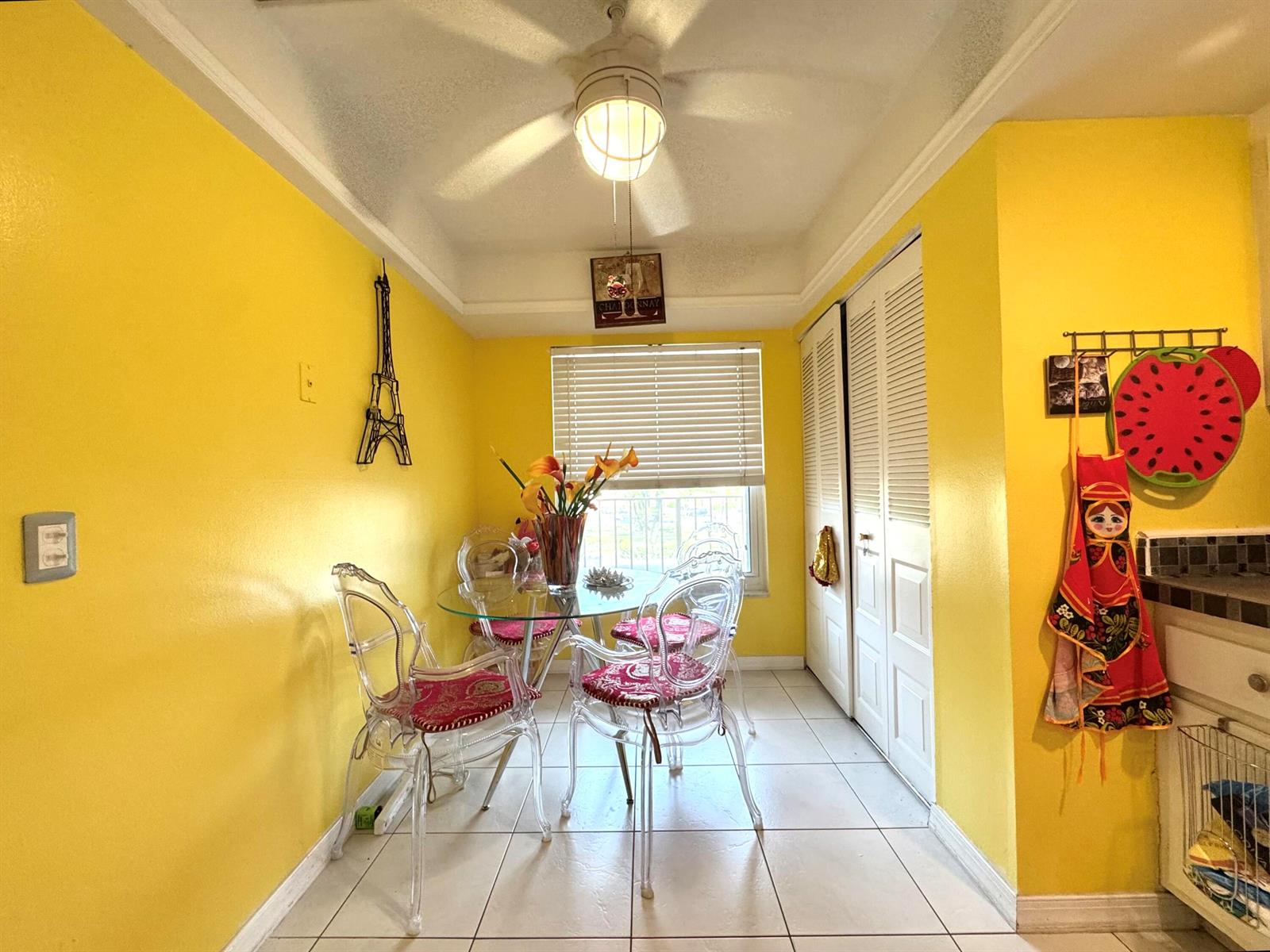 A bright yellow dining area features a glass table, four clear chairs, and tiled flooring — 14671 Bonaire Boulevard # 304, Delray Beach FL 33446, DELRAY BEACH, FL