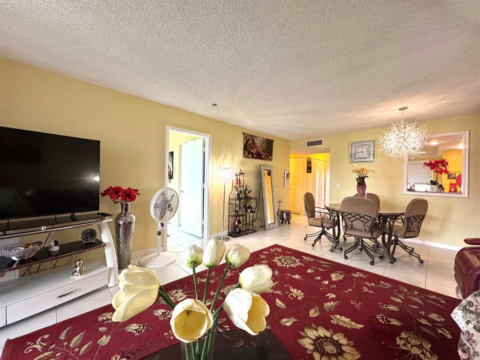 A living and dining area features yellow walls, a red floral rug, and tile flooring — 14671 Bonaire Boulevard # 304, Delray Beach FL 33446, DELRAY BEACH, FL
