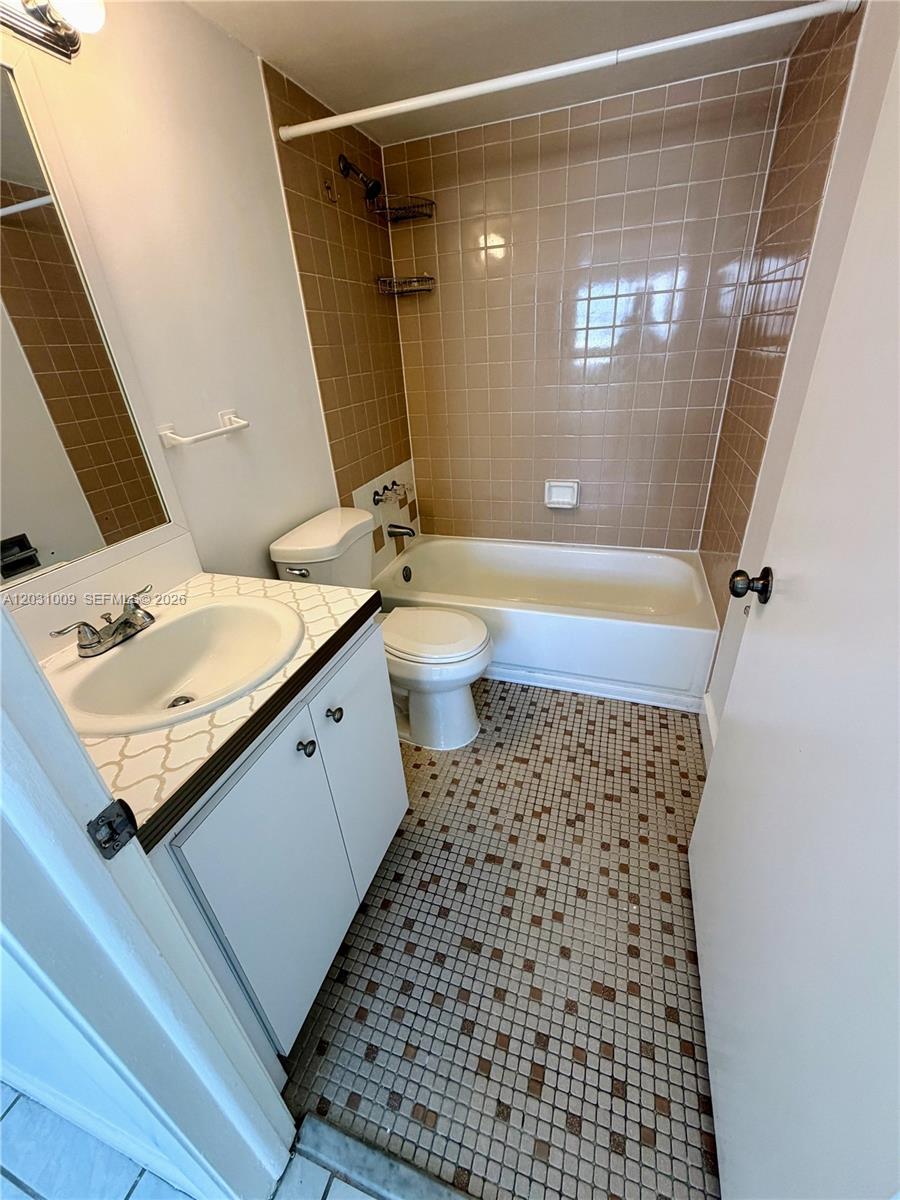 A bathroom features a vanity with a white sink, a toilet, and a tiled tub — 2001 Bay Dr # 401, Miami Beach FL 33141, MIAMI BEACH, FL