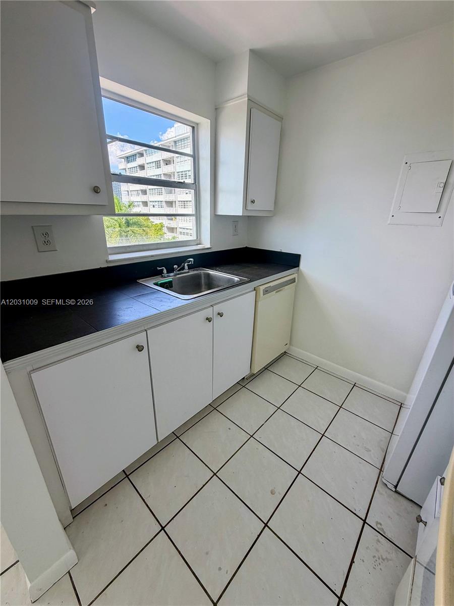 A kitchen features white cabinets, a black tiled countertop, a stainless sink, and tile flooring — 2001 Bay Dr # 401, Miami Beach FL 33141, MIAMI BEACH, FL