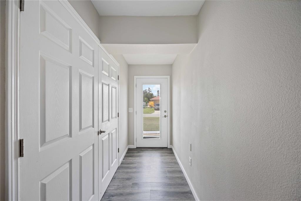 A hallway with gray wood-look flooring, white paneled doors, and a glass-paneled exterior door — 4394 LIBRARY STREET, PORT CHARLOTTE, FL