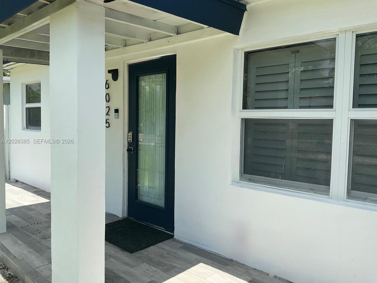 A white exterior wall features a dark blue front door and a large window — 6025 SW 40th St, Miramar FL 33023, MIRAMAR, FL