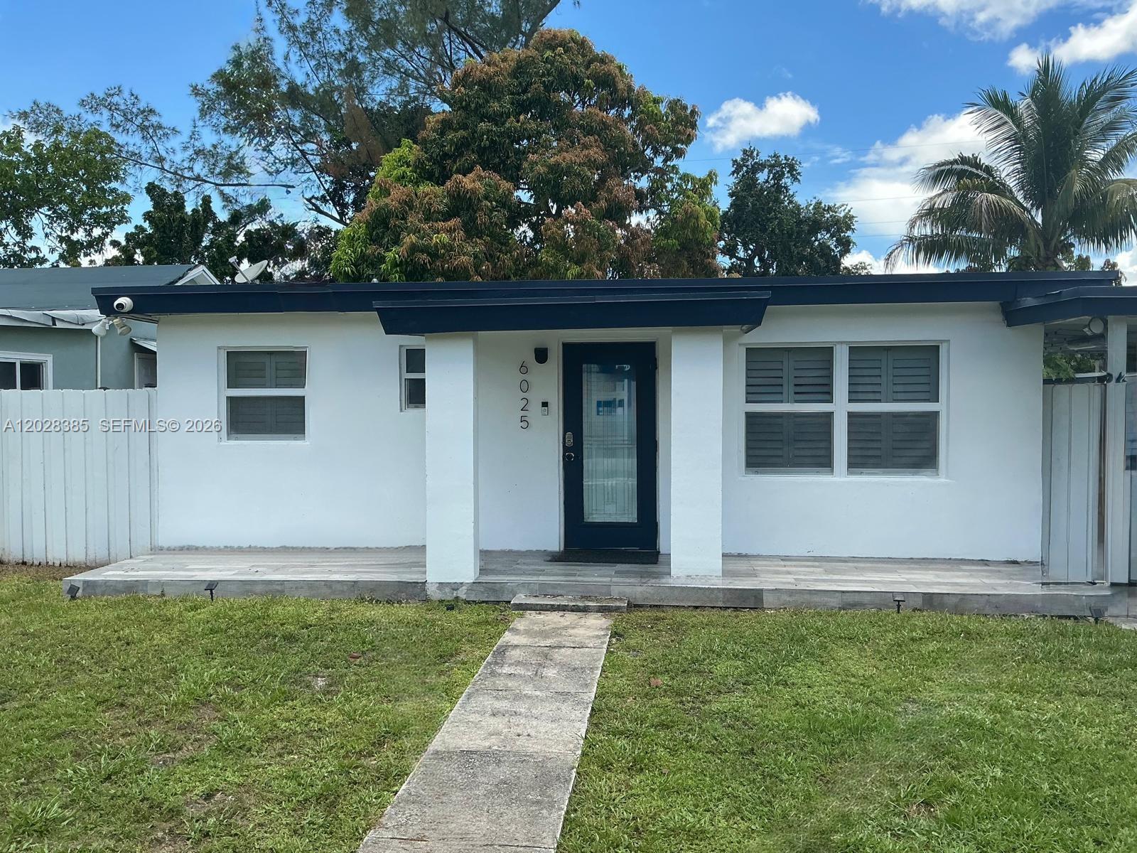 A single-story white house features a dark trim, a front porch, and a walkway — 6025 SW 40th St, Miramar FL 33023, MIRAMAR, FL
